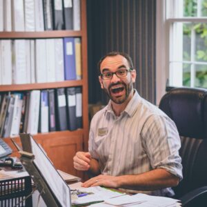 Man with glasses and beard looking excited while working at an office desk.