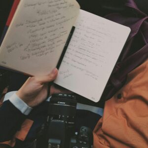 A person holding a notebook with handwritten notes and a camera in view, symbolizing creativity and travel.